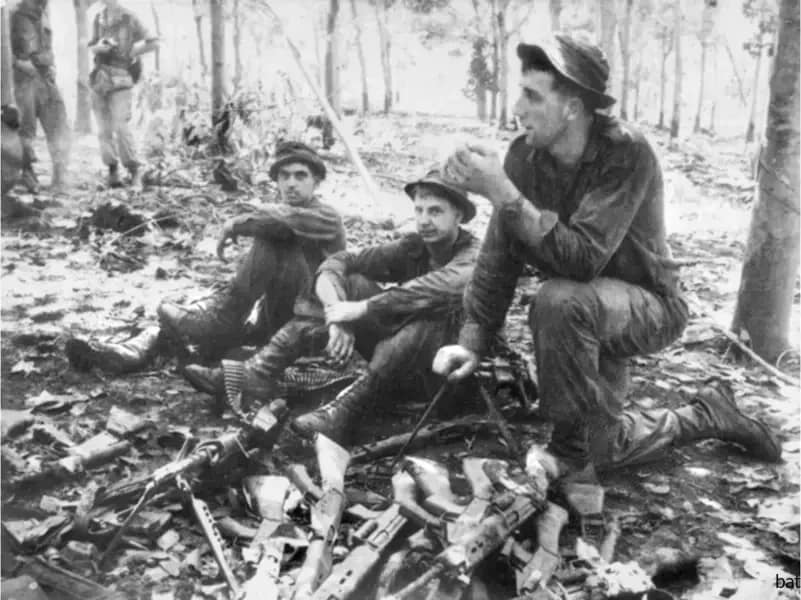 Long Tan, South Vietnam. 19 August 1966. Three soldiers from D Company, 6th Battalion, the Royal Australian Regiment (6RAR), take a break as they gather Australian weapons left on the battlefield after the action of the previous night. Left to right: Private Stan Hodder of Ayr, QLD; Private Terry Burstall of Ballarat, VIC; Private Peter Dettman of Tingha, NSW. @Australian War Memorial