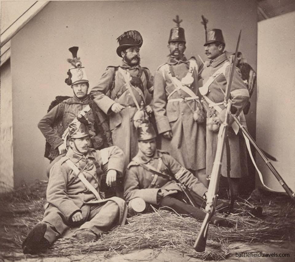 Austrian troops before the battle of Königgrätz. Five infantrymen of the line, one jager (wearing the Tyrolean jager hat), and one hussar (wearing the pelise). Their Model 1854 Lorenz rifle-muskets are stacked beside them.